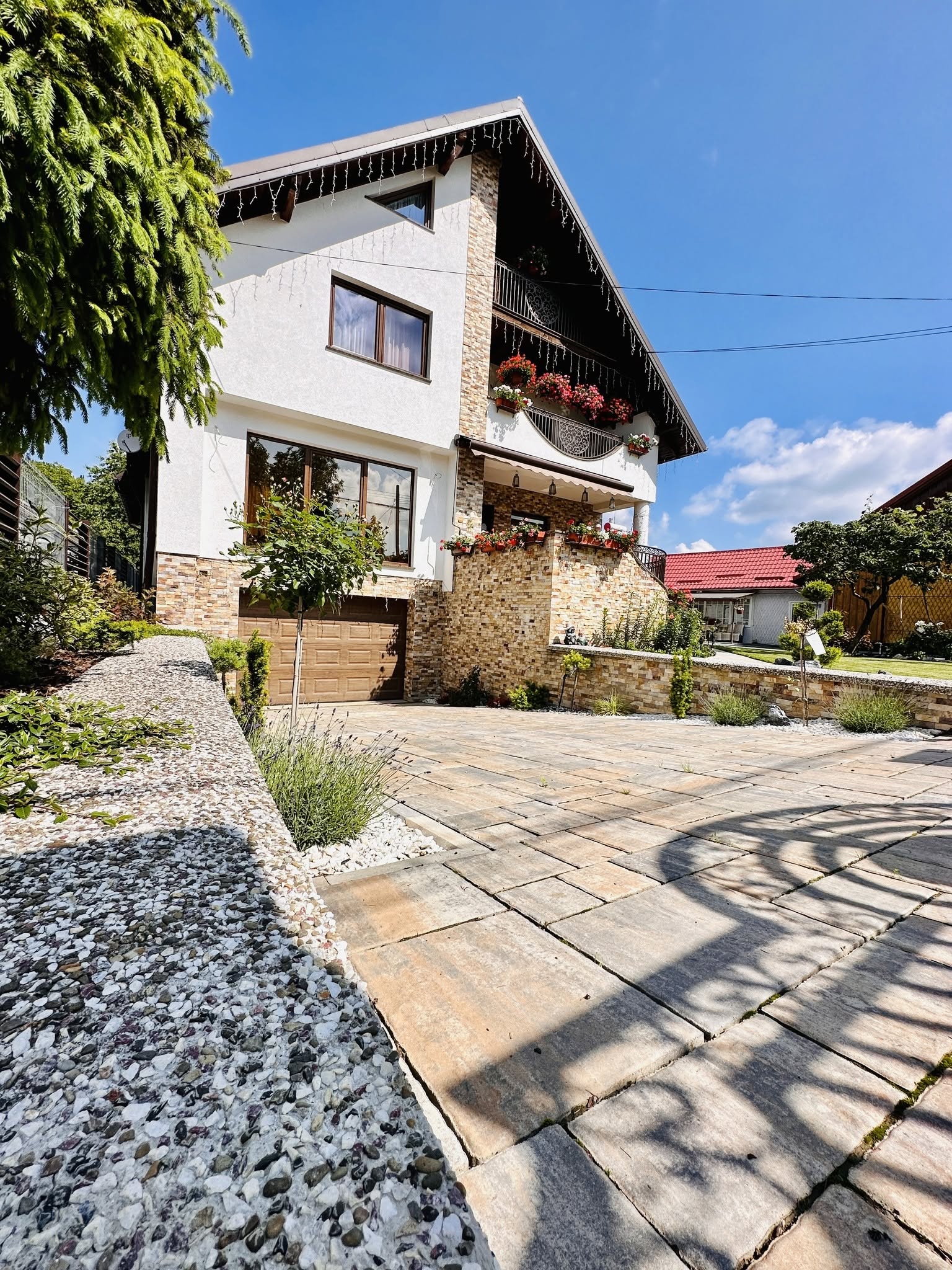 Fațada Casei Alexandra, cu balcoanele pline de flori și aleea pavată din curte