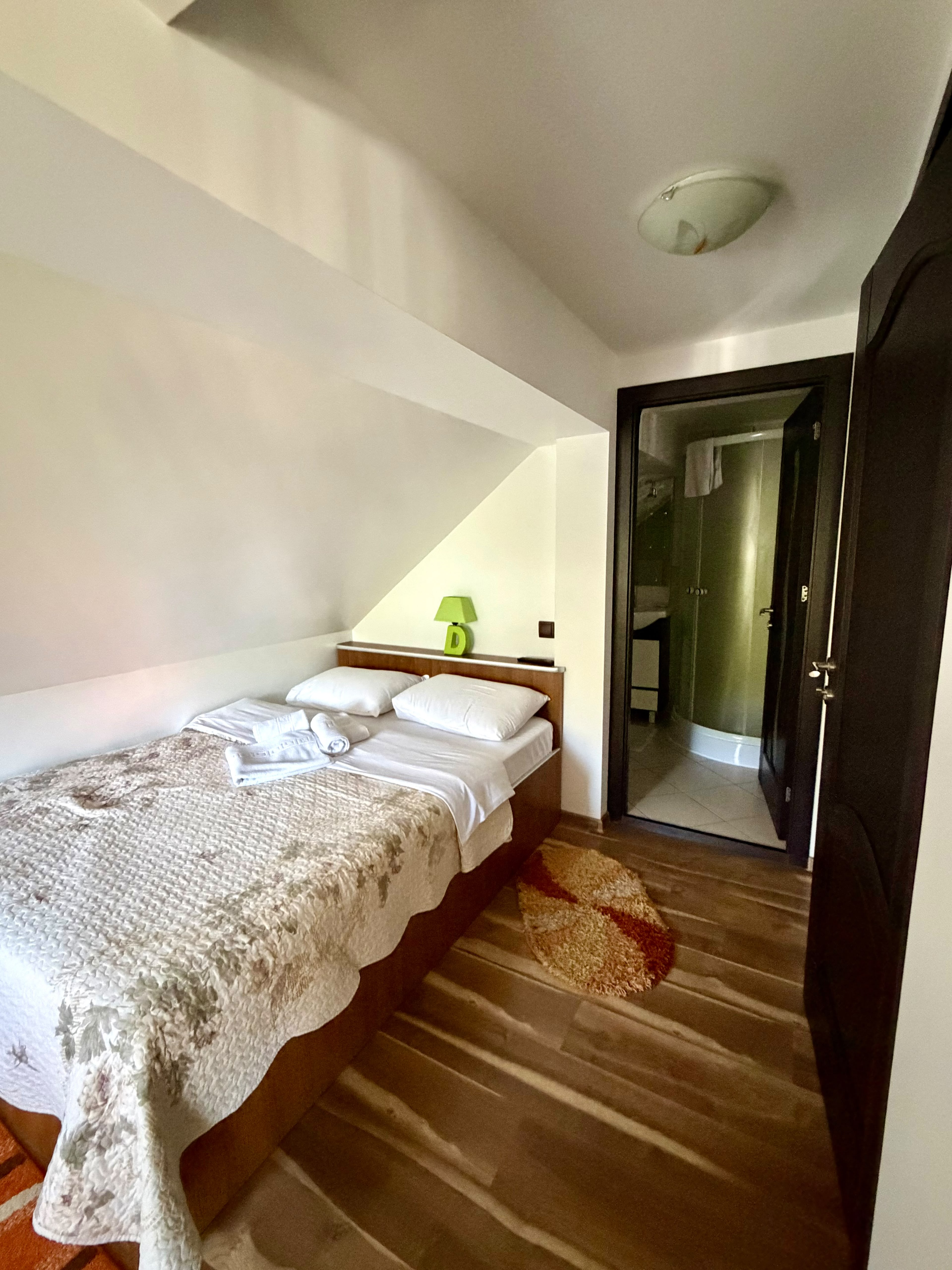 Camera a doua a apartamentului de la mansardă, cu pat matrimonial și intrarea în baia proprie