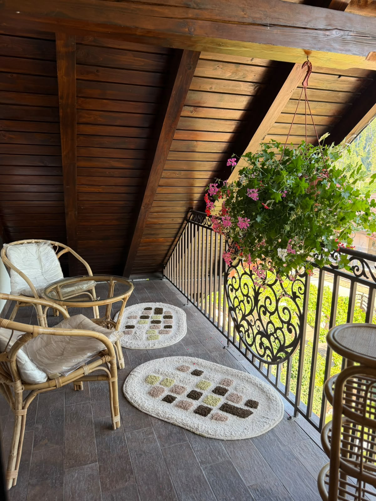 Balconul de la mansardă, cu fotolii de răchită, măsuță de sticlă și o jardinieră suspendată