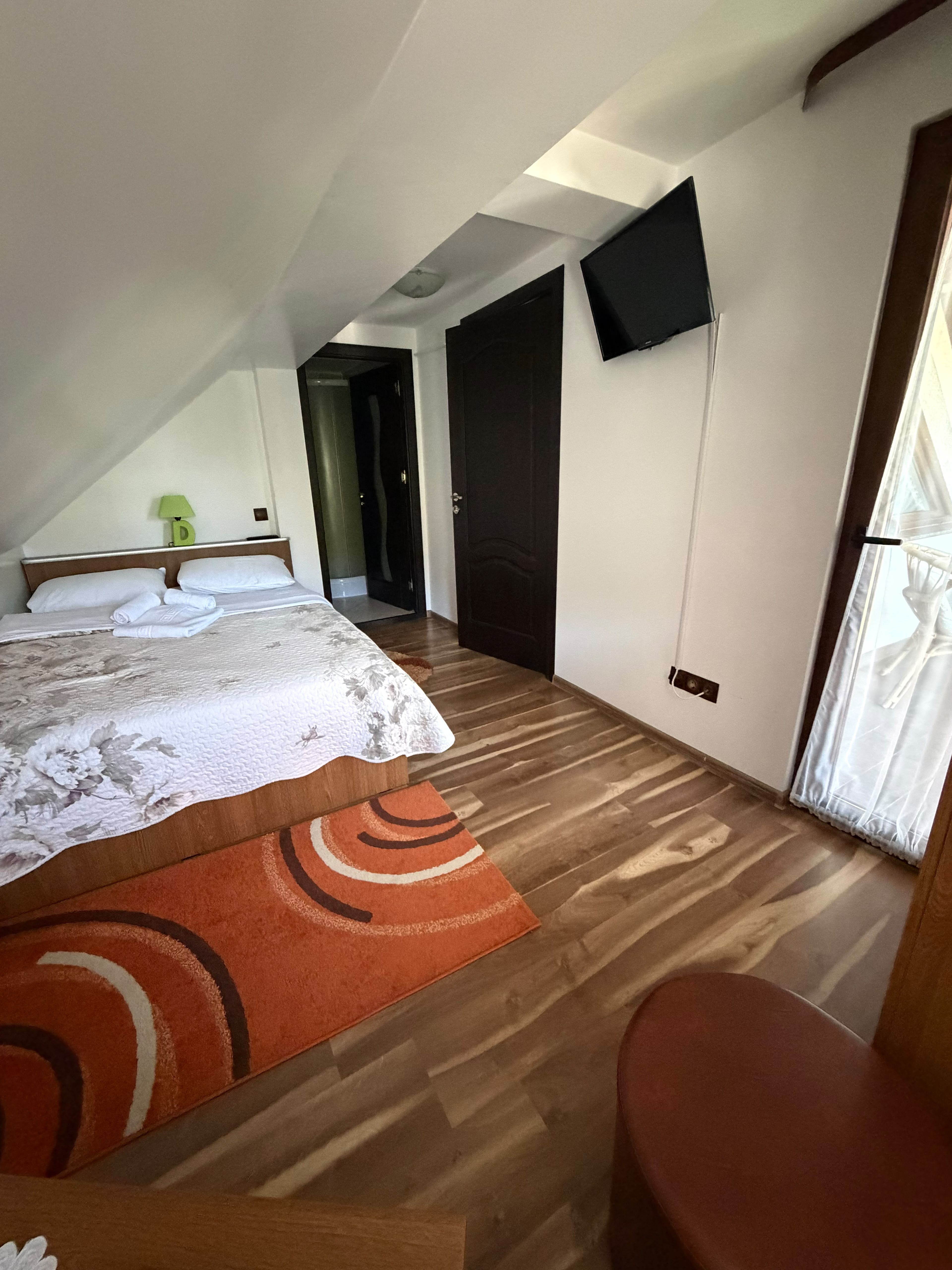Cameră din apartamentul de la mansardă, cu televizor pe perete și fereastră cu perdea