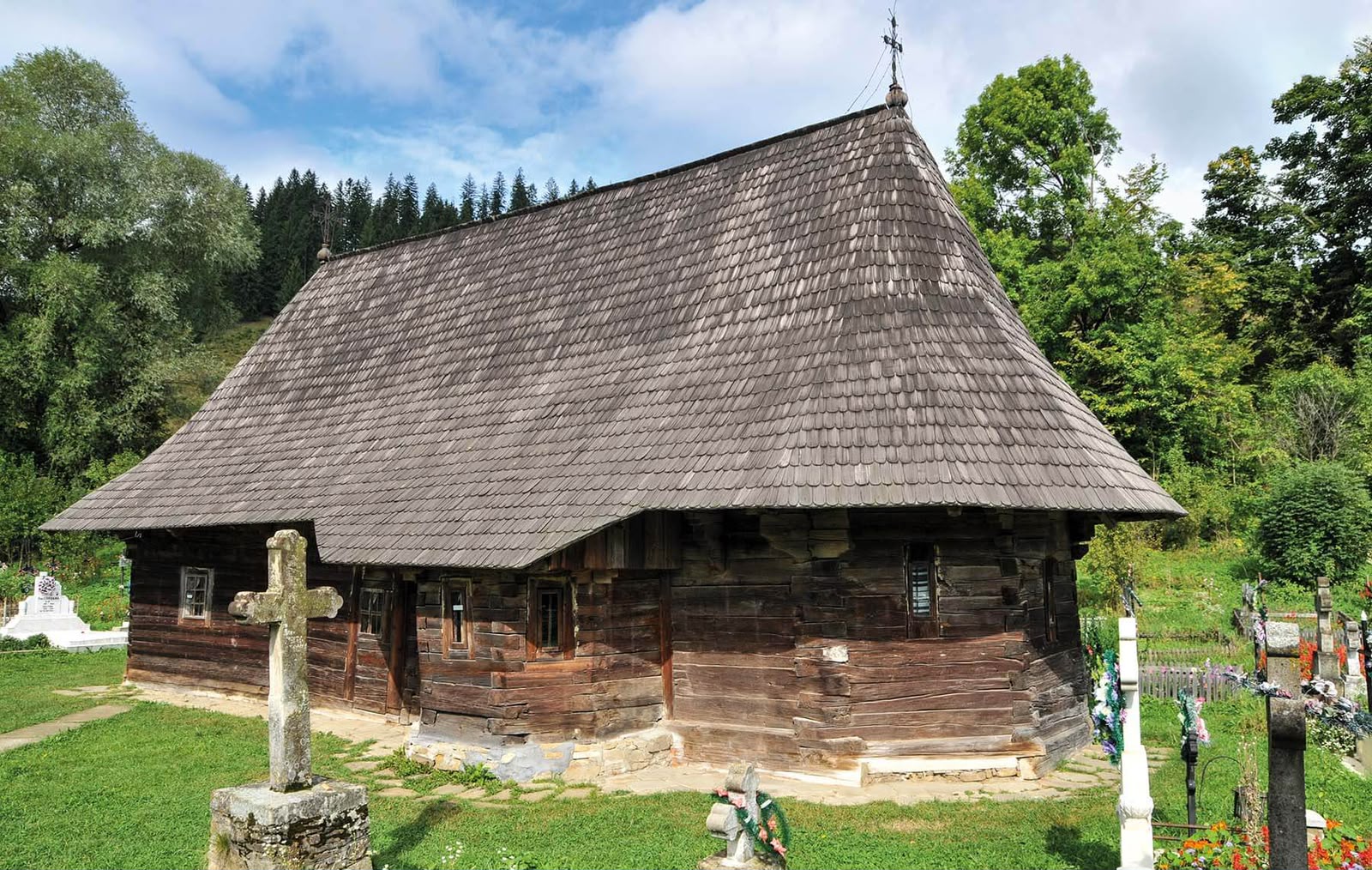 Biserica de lemn Dragoș Vodă din Putna, cu acoperiș de șindrilă și cimitirul din jur