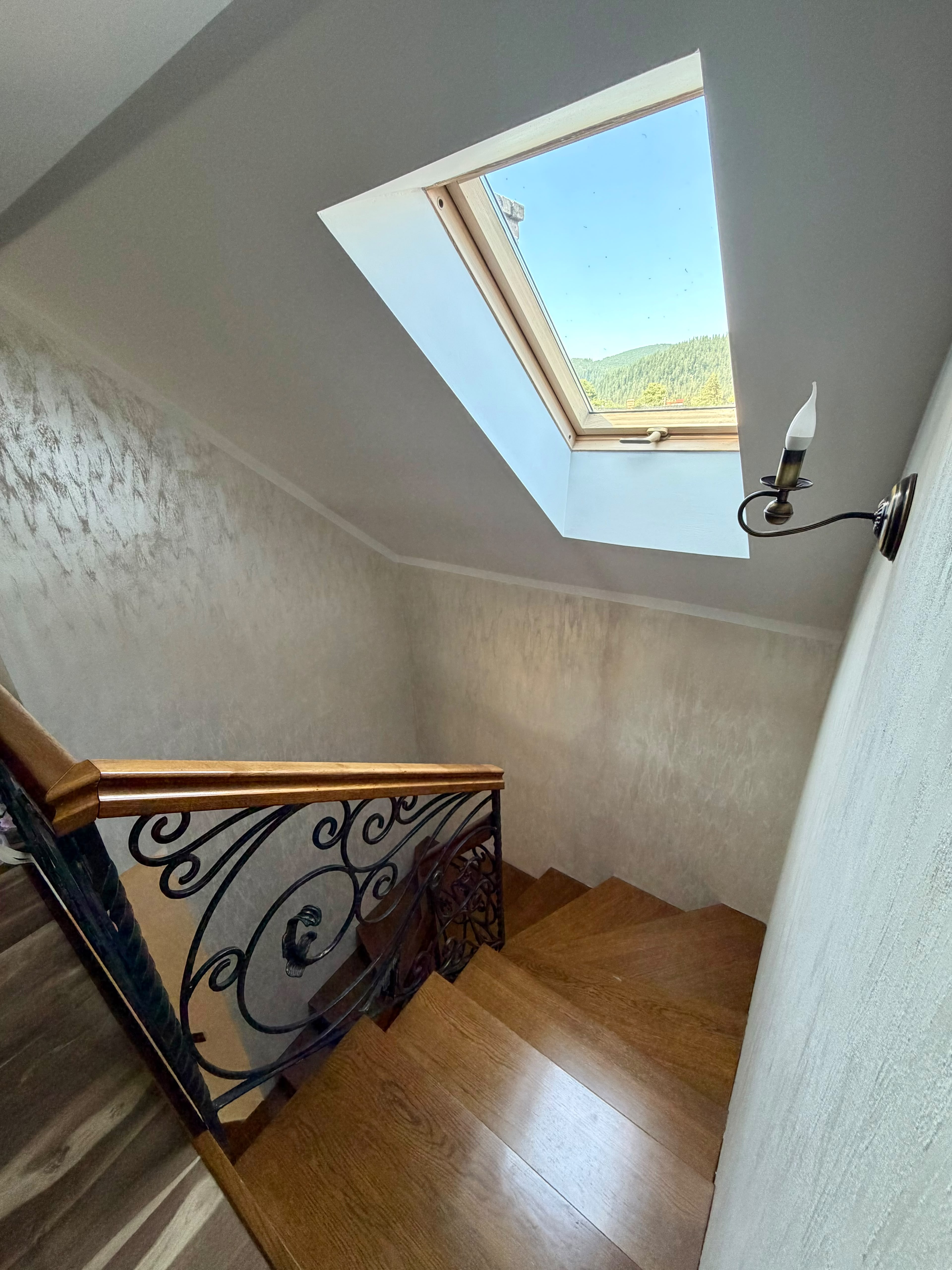 Scara de lemn spre mansardă, cu balustradă din fier forjat și fereastră de mansardă spre dealuri